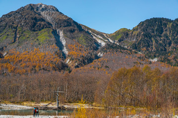 Photos from the back of women standing by the river in Kamikochi, Japan. There are many colorful trees in autumn. Idea of traveling with friend backgrounds. There is a copy space on the right and top.