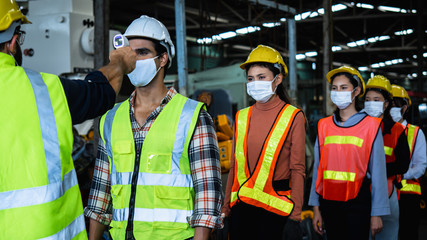 Wall Mural - Industrial worker and engineer stand in line to check flu with infrared thermometer before enter to work and protect Coronavirus or Covid-19, safety and protection as working in manufacturing