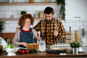 Wall Mural - Young couple making delicious food at home. Loving couple enjoying in the kitchen..