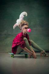blowing bubble with gum on skateboard. young woman as marie antoinette on dark green background. ret