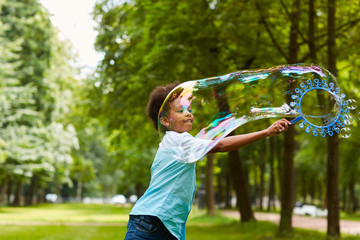 Wall Mural - Waist up portrait of cute African-American boy playing with bubbles outdoors in green park holding big bubble wand, copy space