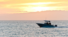 Front View, Far Distance Of A Power Boat Cruising Toward Tropical Harbor At Sunset On Calm Waters Of The Gulf Of Mexico