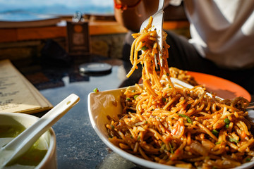 Chef picking up the Schezwan Noodles or Chiken Hakka Noodles or chow mein is a popular Indo-Chinese recipes, served in a bowl or plate with the help of spoon.