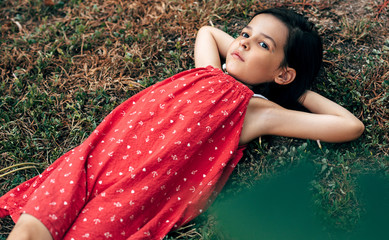 Wall Mural - Top view of cute little girl relaxing on the grass in the park. The kid resting and lying on the grass outdoors during picnic.