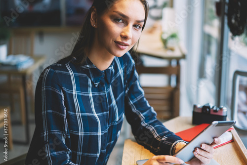 Portrait of attractive brunette female manager doing remote work in cafe interior using application for accountings on tablet, pensive student reading electronic book making researchers for project
