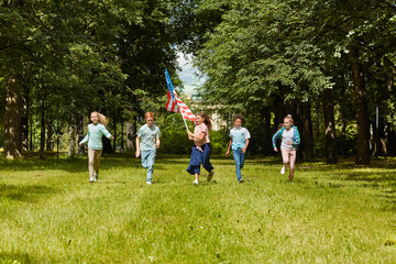 Wall Mural - wide angle view at multi-ethnic group of kids running towards camera across green lawn with girl wav