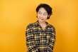 Photo of amazed  Young asian woman with short hair wearing plaid shirt standing over yellow background bitting lip and looking up to empty space, 