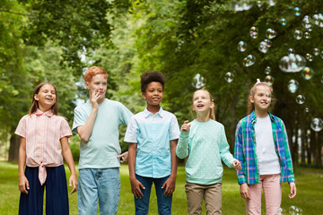 Wall Mural - Front view portrait of multi-ethnic group of kids standing in row outdoors while playing with bubbles in park