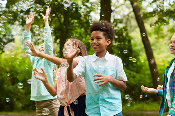 Wall Mural - Waist up portrait of African-American boy and group of carefree children running in park while playing with bubbles outdoors