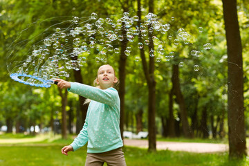 Wall Mural - Waist up portrait of cute girl playing with bubbles outdoors in green park holding big bubble wand, copy space