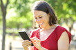 © PheelingsMedia - Happy adult woman texting on phone standing in the park