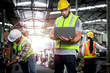 © Stella - Industrial engineer wearing helmet and safe glasses, holding laptop computer for operating machinery at manufacturing plant factory, worker team working together in industry concept