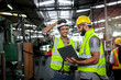 © Stella - Industrial engineer wearing helmet and safe glasses, holding laptop computer for operating machinery at manufacturing plant factory, worker team working together in industry concept