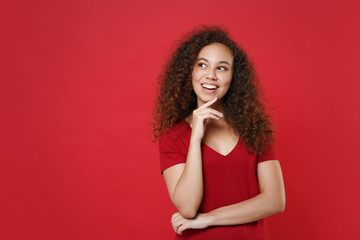 Wall Mural - Pensive young african american woman girl in casual t-shirt posing isolated on red background studio portrait. People lifestyle concept. Mock up copy space. Put hand prop up on chin, looking aside.