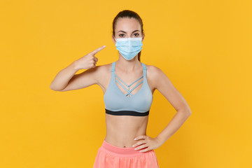 Wall Mural - Young fitness sporty woman in sportswear working out isolated on yellow background studio. Workout sport motivation lifestyle concept. Mock up copy space. Pointing index finger on sterile face mask.