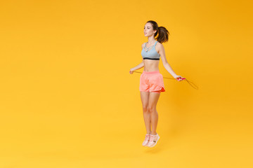 Wall Mural - Full length portrait of attractive young fitness woman girl in sportswear working out isolated on yellow wall background studio. Workout sport motivation lifestyle concept. Jumping with skipping rope.