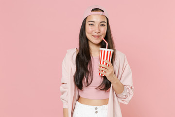 Wall Mural - Smiling young asian woman girl in casual clothes cap posing isolated on pastel pink background studio portrait. People sincere emotions lifestyle concept. Mock up copy space. Hold cup of cola or soda.