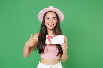 Wall Mural - Smiling young asian woman girl in casual pink clothes hat posing isolated on green wall background in studio. People lifestyle concept. Mock up copy space. Hold gift certificate, showing thumb up.