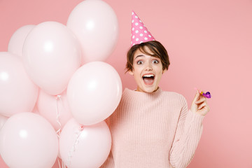 Excite young brunette woman girl in knitted casual sweater birthday hat isolated on pastel pink background. Birthday holiday party people emotions concept. Celebrating hold air balloons hold pipe.