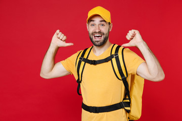 Wall Mural - Delivery employee man guy male 20s in yellow cap t-shirt uniform thermal bag backpack with food work as courier isolated on red background studio. Service during quarantine coronavirus covid-19 virus.