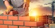 Bricklayer constructor lays bricks on architecture background