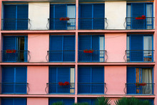Balconies, Flower Decorations And Windows With Closed And Open Blue Shutters In An Apartment Building.