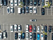 Aerial top view of parking lot at shopping mall with varieties of colored vehicles. People walking to their car and trying to park.
