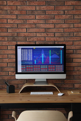modern computer with statistic information on wooden table near brick wall