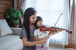 © Odua Images - teenage girls help a child hold the violin bow properly while playing the violin indoors against the background of the window