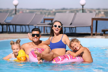 Happy family with inflatable rings in outdoor swimming pool on sunny summer day