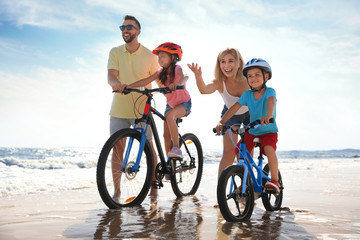 Sticker - Happy parents teaching children to ride bicycles on sandy beach near sea