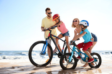 Sticker - Happy parents teaching children to ride bicycles on sandy beach near sea