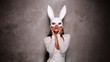Portrait of beautiful flirting Asian woman in white dress and rabbit mask playfully posing for camera in the spotlight