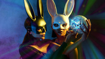 Wall Mural - Portrait of two young cute Asian women in black and white rabbit mask posing with small disco ball on the neon lights