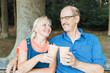 © Alina Rosanova - Senior couple sitting on a park bench, relaxing and drinking coffee to go from bamboo reusable cups. Happy old people, zero waste and sustainable lifestyle concept.
