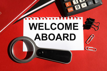 WELCOME WELCOME ON BOARD. TEXT is written on white paper on a red background near the stationery.