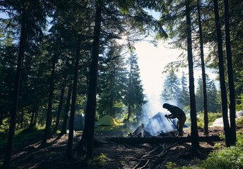 Wall Mural - silhouette of male tourist bending over wooden trunk, breaking branches, trying to make fire near te