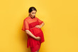 © LIGHTFIELD STUDIOS - pregnant young woman in red tunic touching belly on yellow