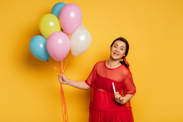 Wall Mural - pregnant woman holding multicolored festive balloons and pregnancy test on yellow background