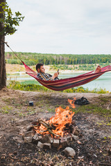 Wall Mural - man laying on hammock at lake beach near camp fire