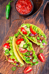 Wall Mural - Taco shells with lettuce, ground beef meat,  mashed avocado, tomato, red onion and jalapeno pepper, on wooden board, vertical, top view