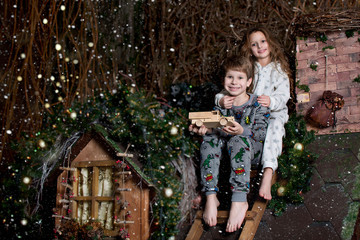 Wall Mural - Little girl and boy sit on a snowy roof at Christmas. Children play on the roof. Children are waiting for santa claus. Christmas tales
