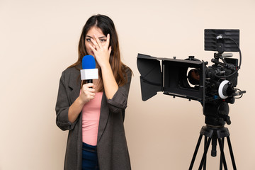 Reporter woman holding a microphone and reporting news over isolated background covering eyes and looking through fingers