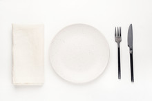 Set Of Black Cutlery Knife And Fork, White Plate And Napkin On A White Wooden Table. Restaurant Or Cafe Concept.