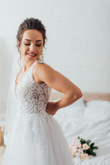 Wall Mural - Young bride in veil putting on wedding dress at home