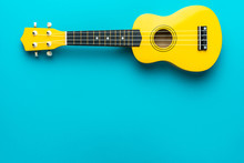 Yellow Colored Wooden Ukulele Guitar On The Turquoise Blue Background. Overhead Photo Of Ukulele With Copy Space.