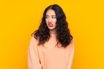 Wall Mural - Spanish Chinese woman over isolated yellow background with confuse face expression