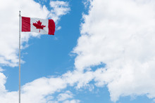 Canadian Flag With Maple Leaf Flying With Blue Sky And Fluffy Clouds