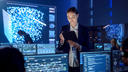 Fototapete - Female Project Leader is Standing with Tablet Computer and Checking Work Data. Science Engineers Work Around Her. Telecommunications Control Monitoring Room with Neural Network on Big Screen.