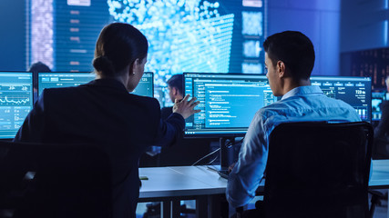 Fototapete - Confident Female Data Scientist Works Closely to her Young Colleague in Big Control and Monitoring Room with Neural Network. Young Specialists Talk and Discuss Work in a Room with Other Employees.